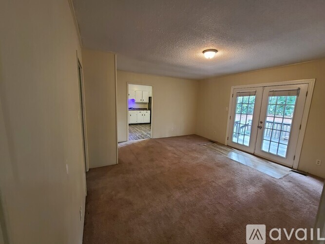 A room with a carpeted floor and a window with a view of trees.