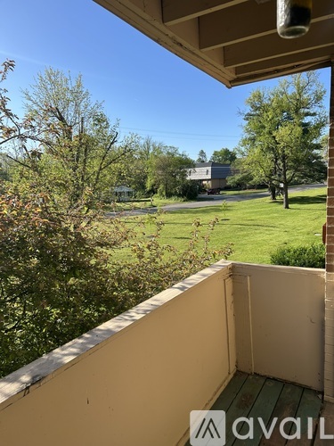 A balcony with a view of a green lawn and trees.