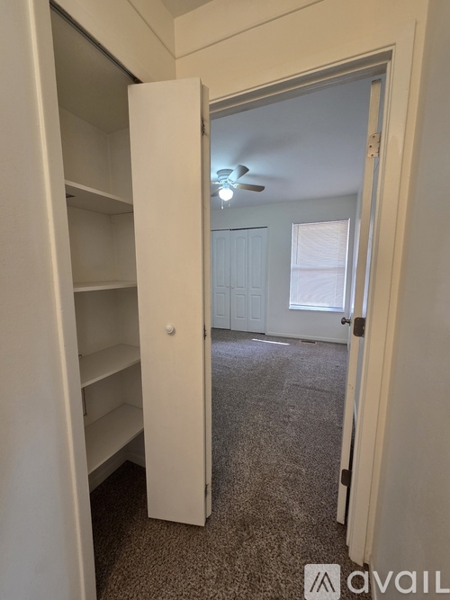A white closet with an open door leading to a bedroom.