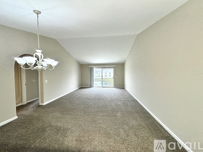 A well-lit, empty room with a chandelier and carpeted floor.