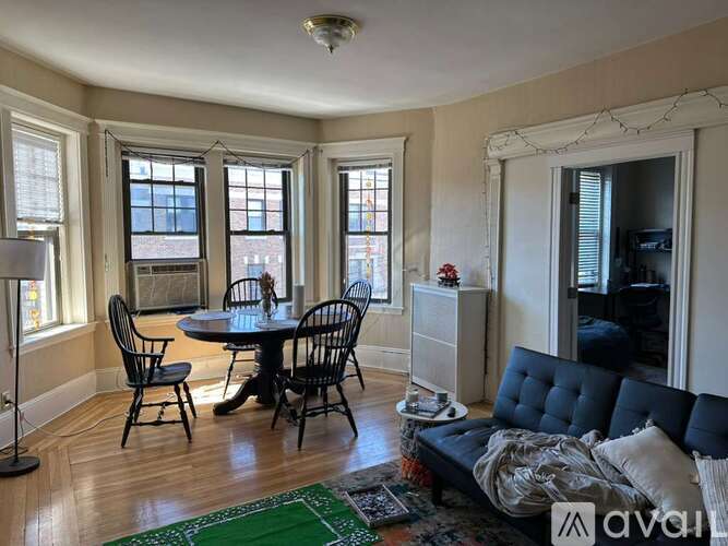 A living room with a black couch, a round table with four chairs, and a green rug.