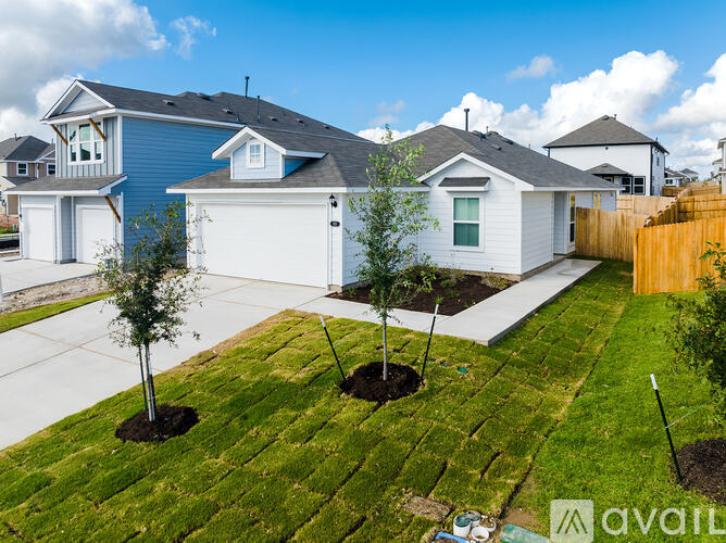 A house with a blue roof and white walls is surrounded by a white fence and has a small garden in front.