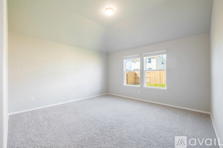 A room with a carpeted floor and a window showing a wooden fence and a building outside.