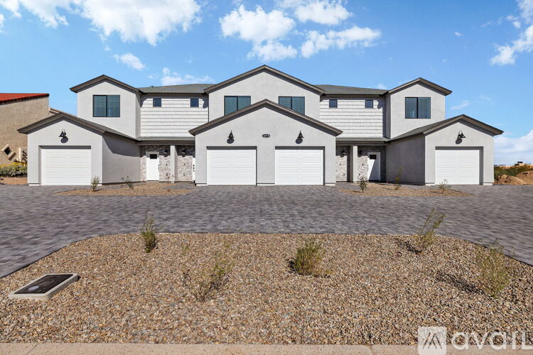 A large, modern house with a grey roof and white walls, featuring a driveway and a gravel area in front.