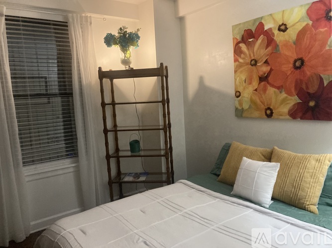 A bedroom with a bed, a wooden ladder, a vase with flowers, and a painting of flowers on the wall.