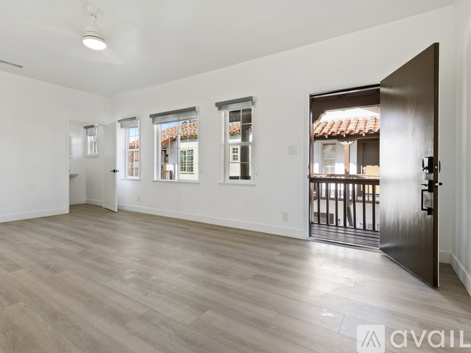 A spacious room with wooden flooring and a view of a building through the windows.