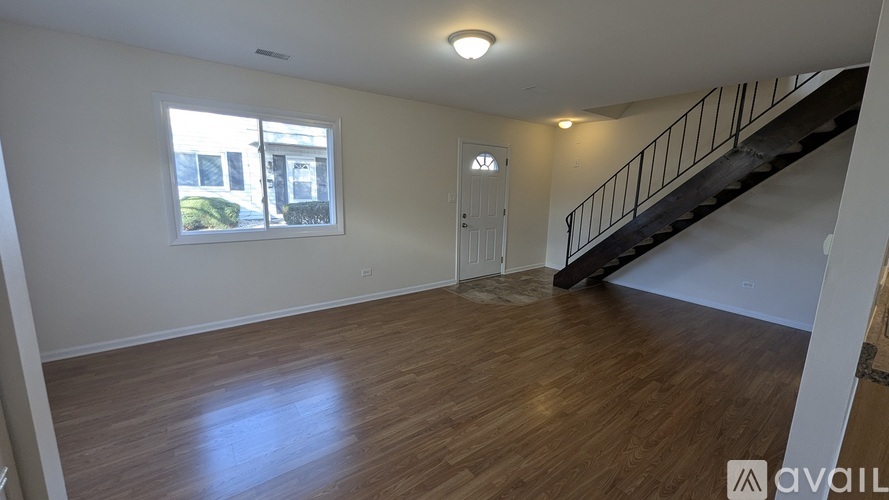 A spacious room with wooden floors and a staircase with a metal railing.