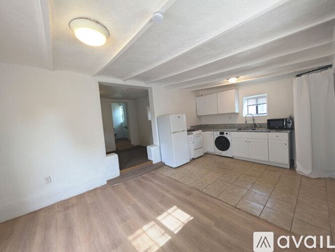 A kitchen area with white cabinets and appliances, and a wooden floor.
