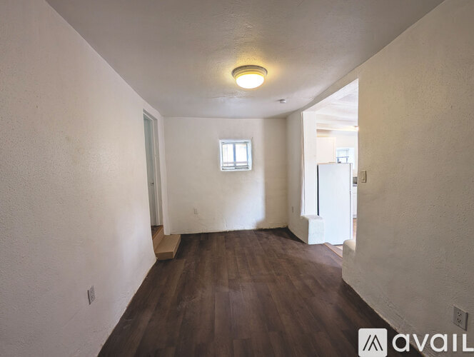A room with wooden floors and white walls, with a window and a door visible.