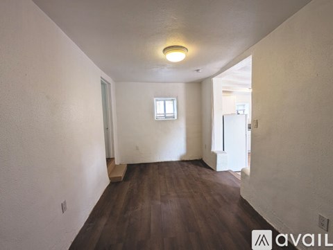 A room with wooden floors and white walls, with a window and a door visible.