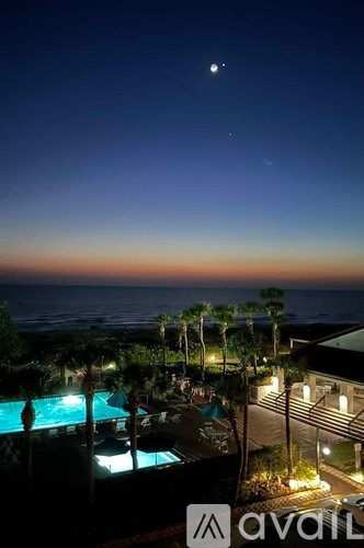 A pool at night with a view of the ocean and a moon in the sky.