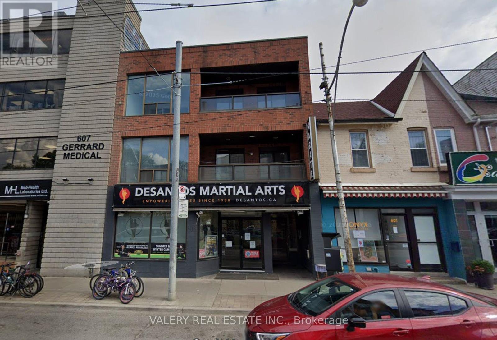 A street view with a red car parked in front of a building with a sign that reads "Designs Martial Arts".