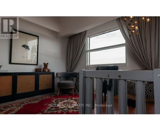 A living room with a grey crib in the foreground and a large window with curtains.
