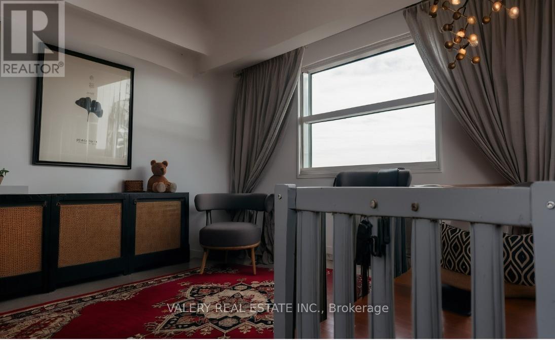 A living room with a grey crib in the foreground and a large window with curtains.