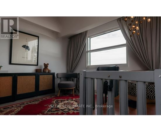 A living room with a grey crib in the foreground and a large window with curtains.