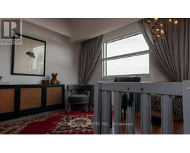 A living room with a grey crib in the foreground and a large window with curtains.