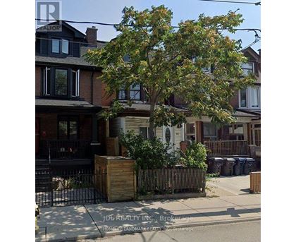 A tree in front of a house with a sign that says JOREALTY INC Brokerage.