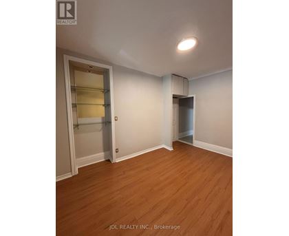 A room with wooden floors and white walls, with a door on the left and a closet on the right.