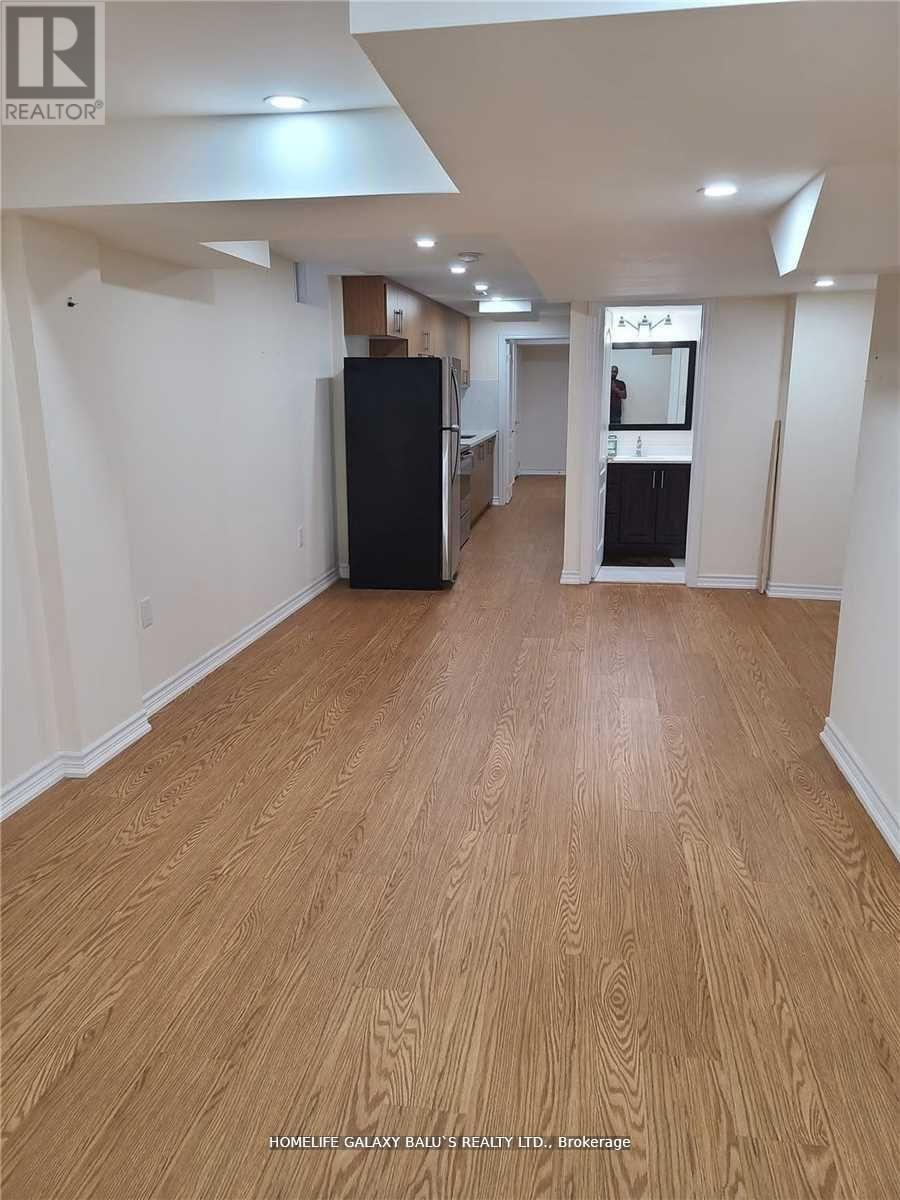 A spacious room with wooden flooring and a black refrigerator.