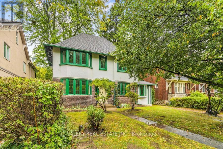 A house with green shutters and a white door is surrounded by trees and bushes.