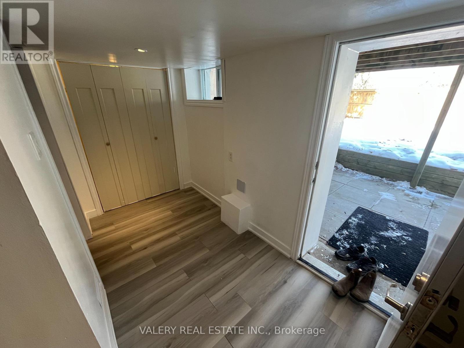 A room with wooden flooring and white walls, with a view of a snowy outdoor area through a glass door.