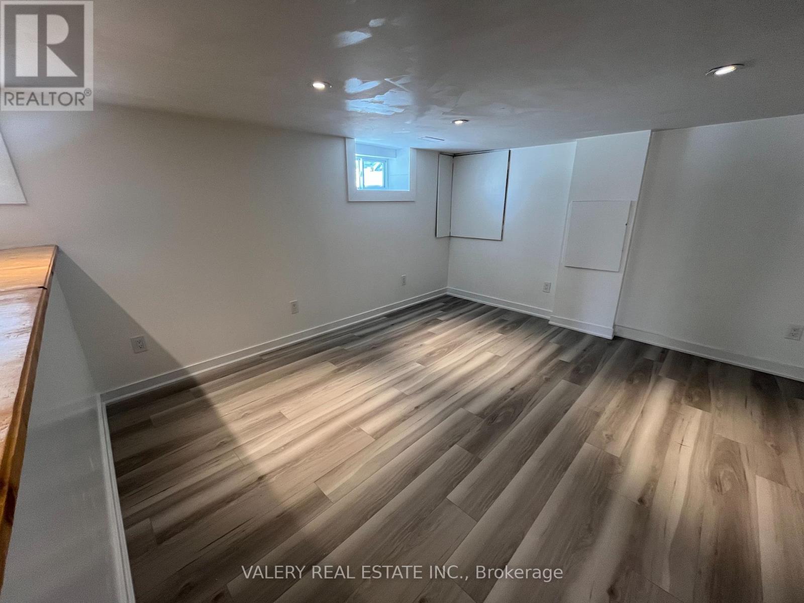 A room with wooden flooring and white walls, with a window and a door on the right side.