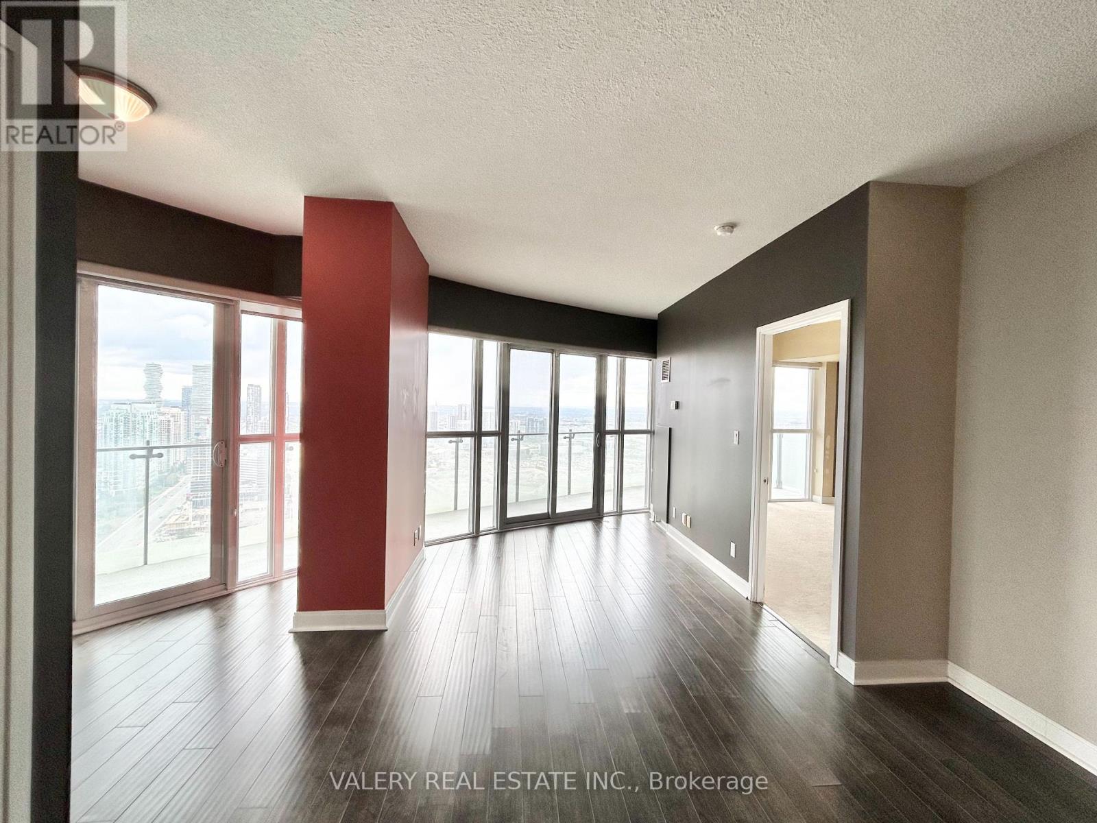 A spacious room with wooden floors and large windows.