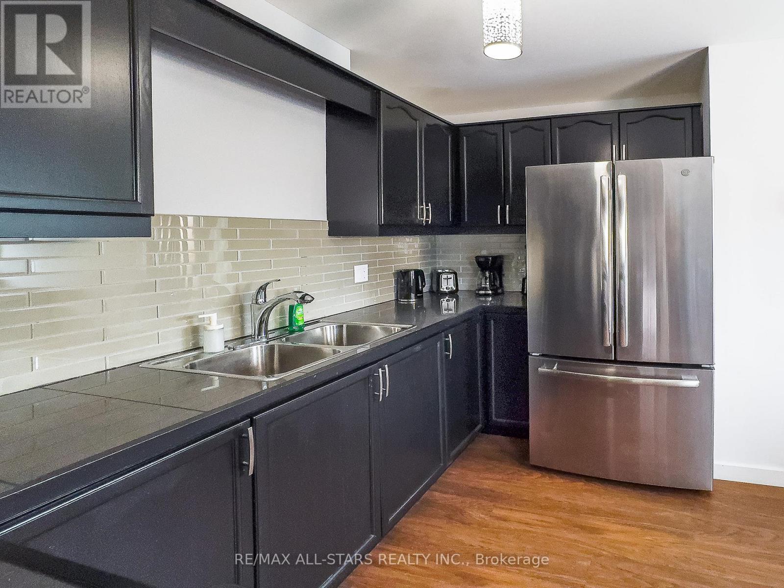 A kitchen with black cabinets and a stainless steel refrigerator.