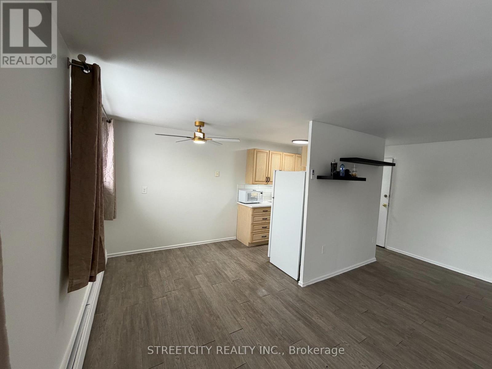A room with a ceiling fan and a refrigerator in it.
