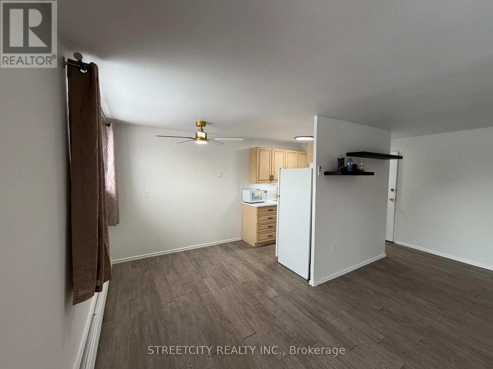 A room with a ceiling fan and a small kitchenette.
