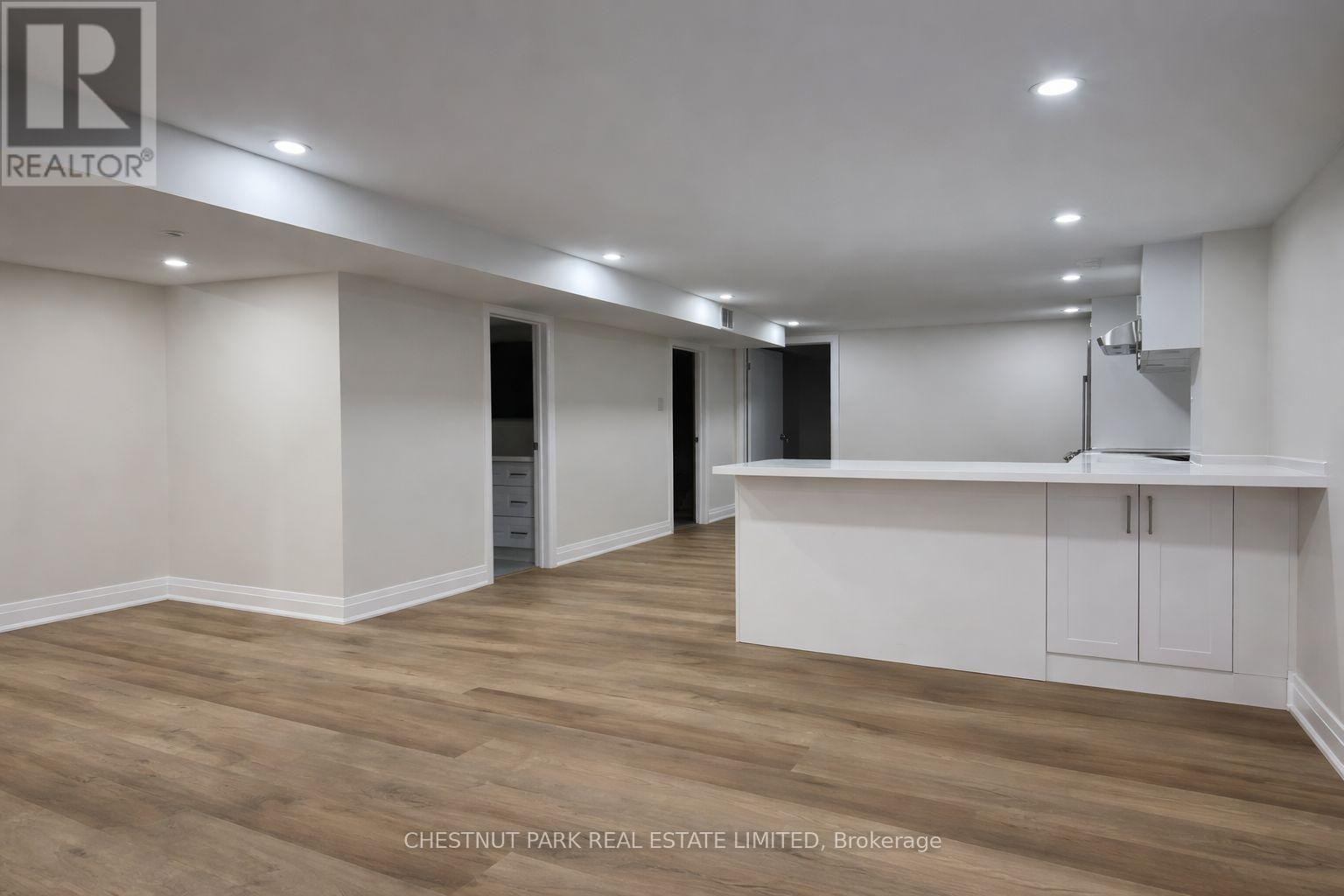 A spacious room with wooden flooring and white walls, featuring a kitchenette with a sink and cabinets.