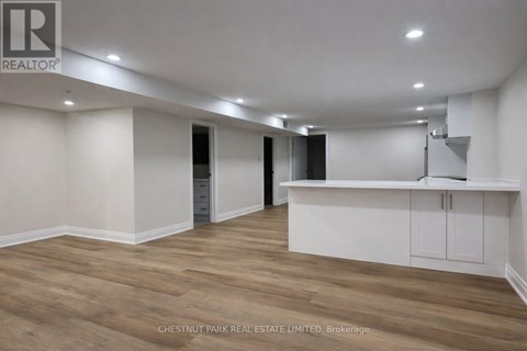 A spacious room with wooden flooring and white walls, featuring a kitchenette with a sink and cabinets.
