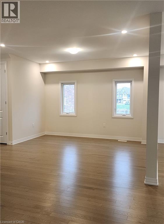 A spacious room with wooden flooring and two windows.