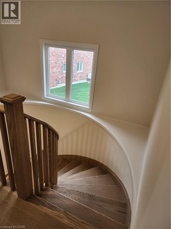 A spiral staircase with wooden steps and railings leads up to a window with a view of a red brick building.