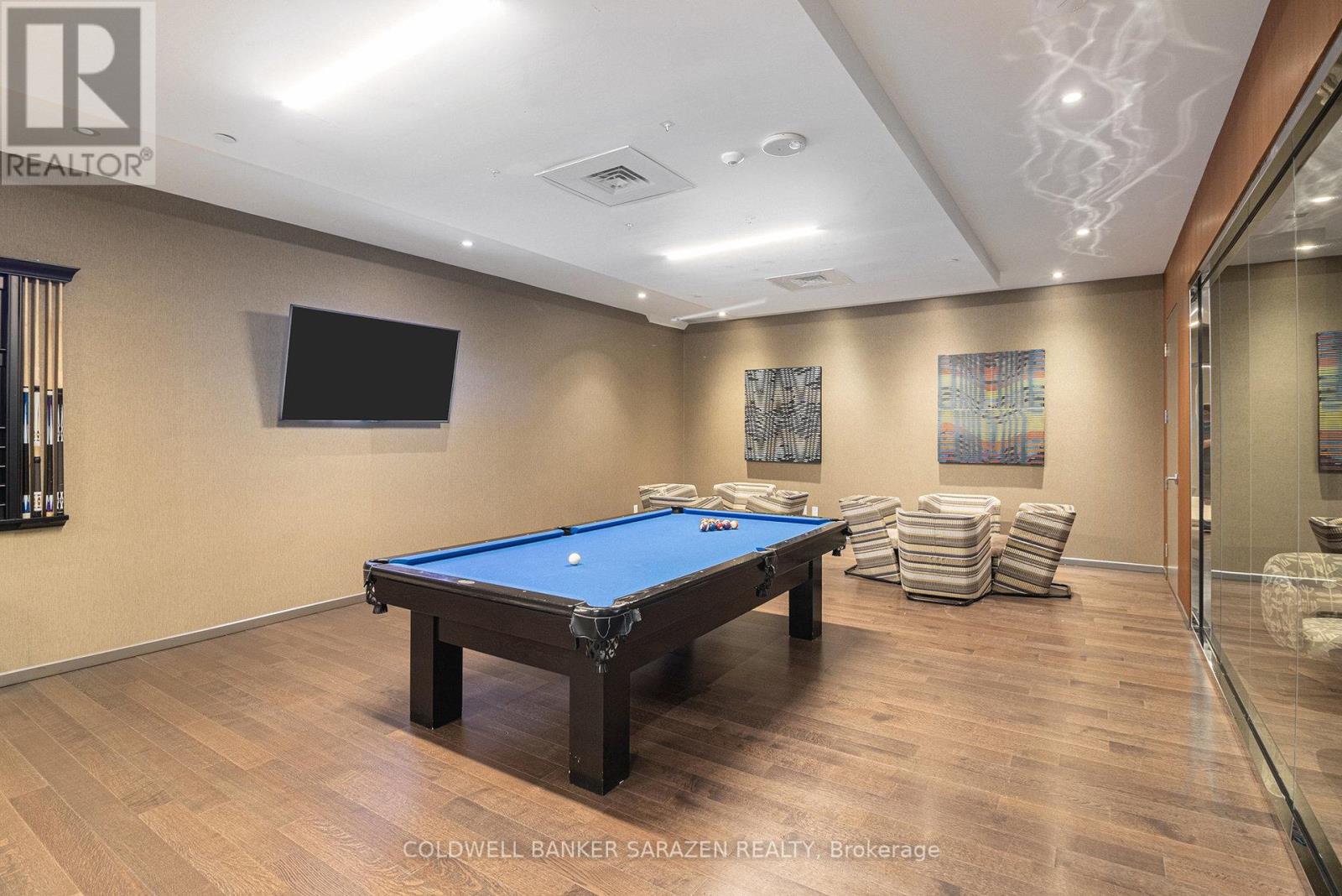 A pool table in a room with wood flooring and a television mounted on the wall.