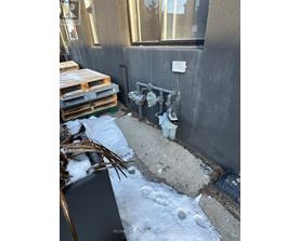 A dirty outdoor area with a pipe and a white bucket.