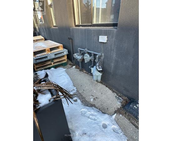 A dirty outdoor area with a pipe and a white bucket.