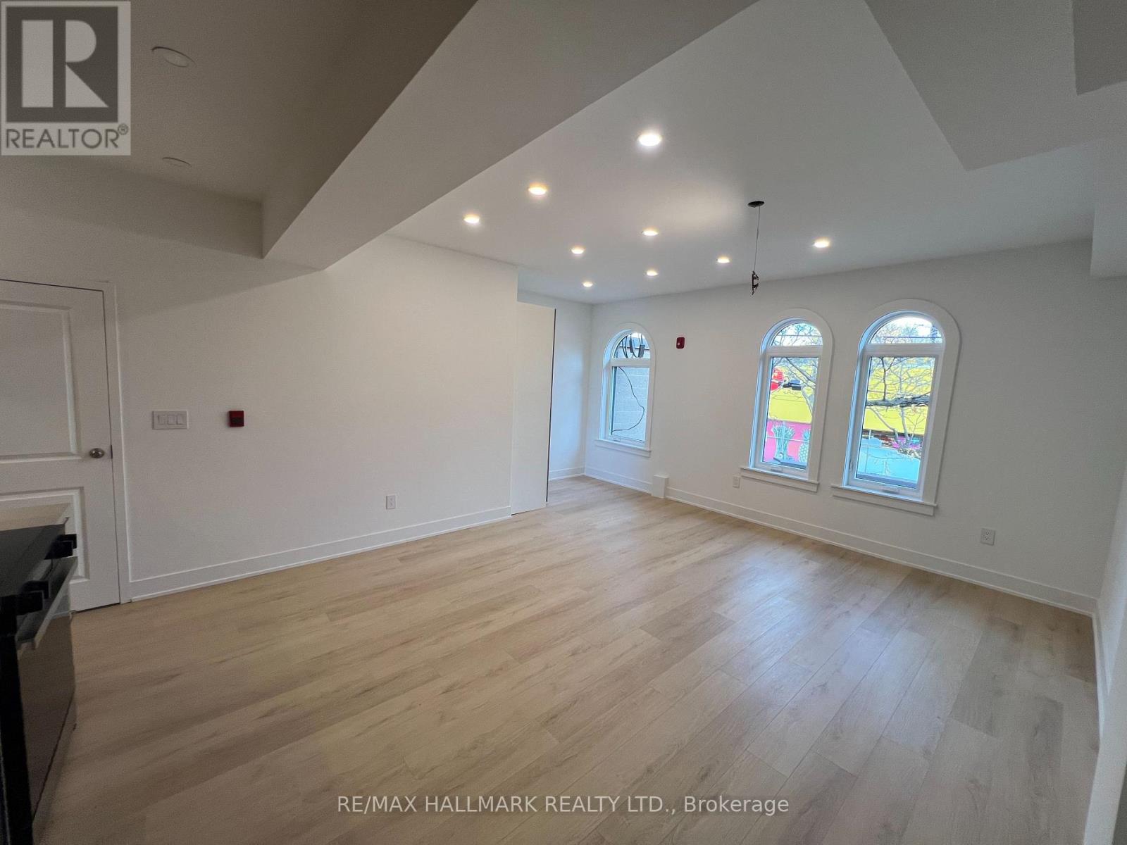 A spacious room with wooden flooring and three windows.