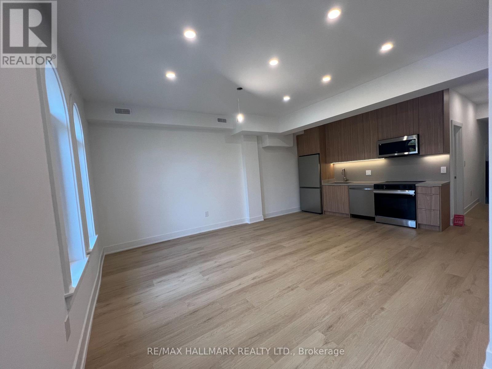 A spacious room with wooden flooring and a kitchen area with stainless steel appliances.
