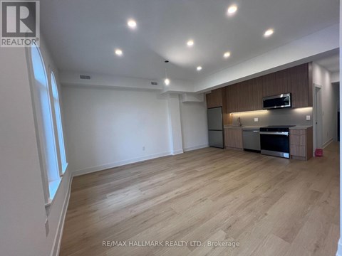 A spacious room with wooden flooring and a kitchen area with stainless steel appliances.