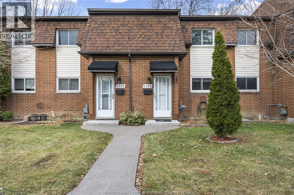 A brick house with a white door and a small tree in front.