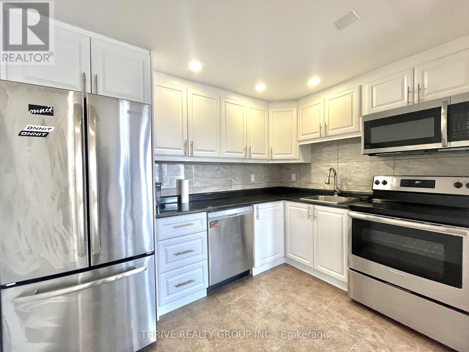 A kitchen with a refrigerator, microwave, oven, and sink.