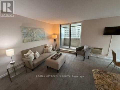A living room with a grey couch, a white chair, and a painting on the wall.