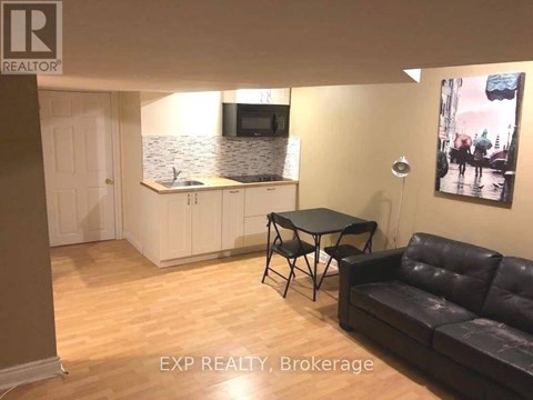 A living room with a black leather couch, a small table, and a painting on the wall.