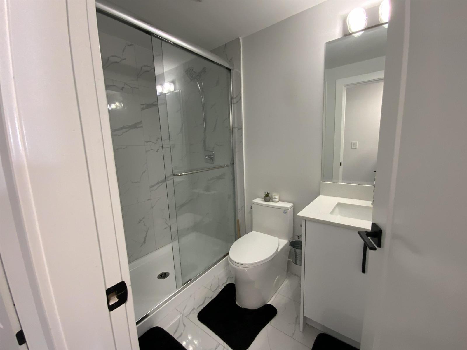 A white toilet with a black mat in front of a glass shower stall.