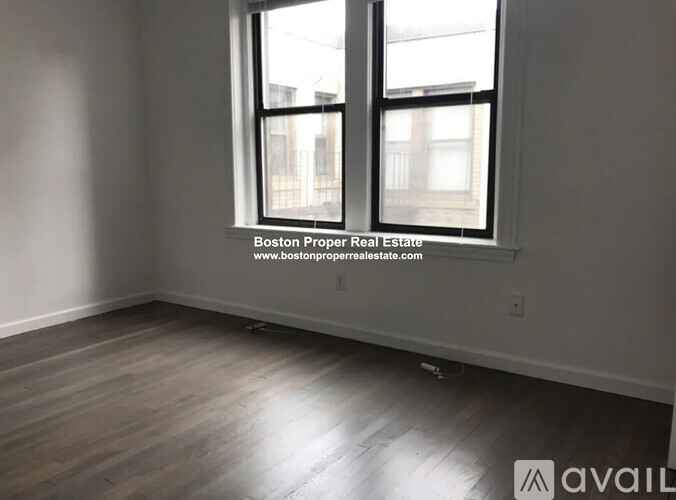 A room with a large window and wooden flooring is available for rent.