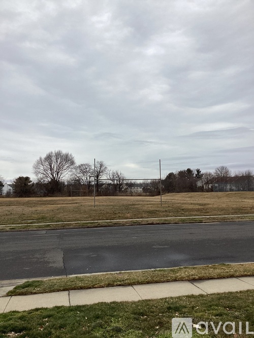 A road with a sidewalk and grassy field with trees in the background.