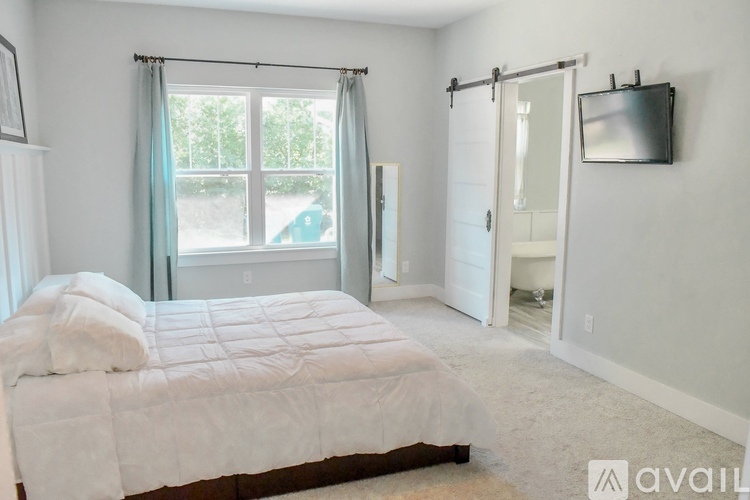 A bedroom with a bed, a window with curtains, and a sliding glass door leading to a balcony.