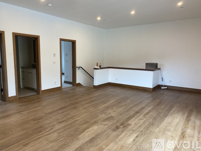 A spacious room with wooden flooring and white walls.