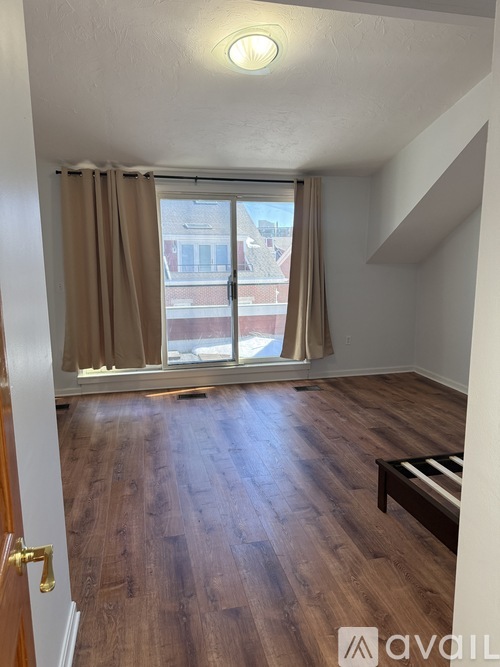A room with wooden flooring and a window with curtains.